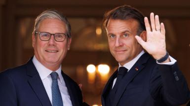 UK Prime minster Sir Keir Starmer and French President Emmanuel Macron stand in the doorway of number 10 Downing Street. President Macron is waving.