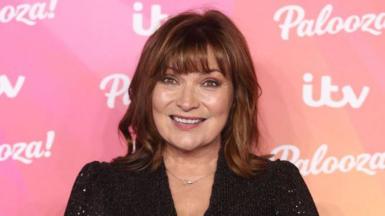 Lorraine Kelly in front of a pink branded background covered in logos