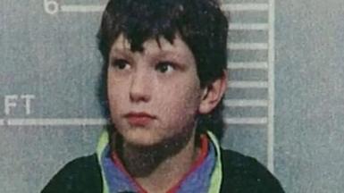 A police custody shot of a young Jon Venables, wearing a dark jumper, after his arrest. He is standing in front of a height chart showing he stands just over 4ft 6in tall. 