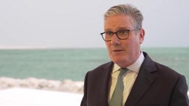 Keir Starmer wearing a suit standing in front of the sea
