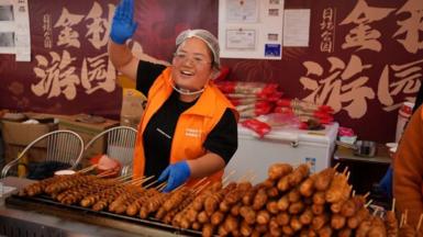 Woman working on food stall waving at someone off camera