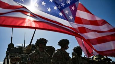 US Army soldiers stand in formation next to a US flag and a US Army armoured vehicle as they take part in the NATO "Noble Blueprint 23" joint military exercise at the Novo Selo military ground, northwestern Bulgaria, on September 26, 2023.