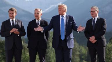 Four men - French President Emmanuel Macron, Canadian Prime Minister Mark Carney, US President Donald Trump and British Prime Minister Keir Starmer - pose for a photo with a mountainous backdrop behind them.