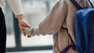 A boy wearing a backpack holding a woman's hand.