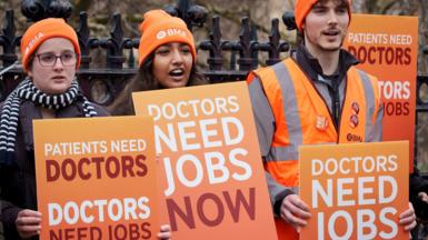 BMA resident doctors hold placards reading 'doctors need jobs now' while striking in London in December
