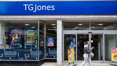 A woman walks in front of a TG Jones store front.