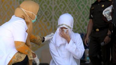 Health workers examine a woman during the legal process of flogging a violator of Islamic law with a sentence of 140 lashes in Aceh, Indonesia.