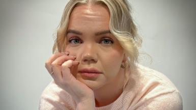 Meri-Tuuli Auer looking towards the camera, she is seated with her head resting in her hand. She has blond hair and is wearing a light pink short sleeved woollen top.
