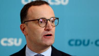 Jens Spahn speaks with German media during a party meeting, he is wearing a black suit and black glasses.