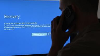 Man looks at Microsoft Blue Screen of Death on desktop while talking on the phone
