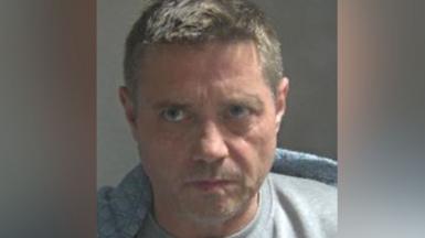A custody photo of John Alford wearing a grey T-shirt or jumper.