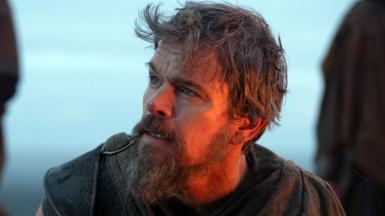 Matt Damon pictured in the Odyssey against a blue sky