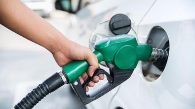  A close up of a person's hand holding a petrol pump as they fill up their white car