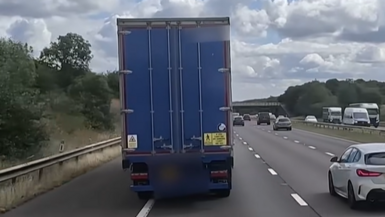 A blue lorry swerving into the hard shoulder lane on a motorway.