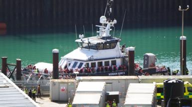 A large white boat docked. It is filled with people.