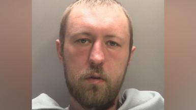 A mug shot of John Ashby who has short light brown hair and facial hair. he has a grey blanket across his front