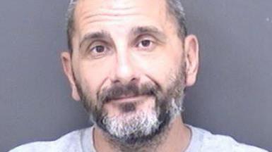 A custody shot of Matthew Ashley Foster-Smith. He has short hair and a beard and is wearing a grey jumper. 