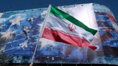 The Iranian flag is pictured being waved in the air in front of a building with a mural depicting an Iranian misssile attack on a US carrier in the gulf, in Tehran's Revolution Square on 1 March.