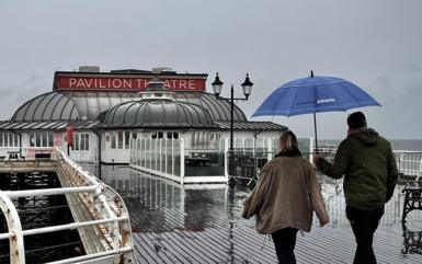 A couple with an umbrella walk along a wet Cromer pier under a grey sky
