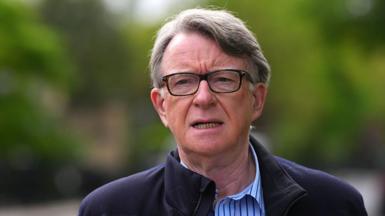 Lord Mandelson in glasses and a blue striped shirt 