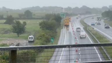 Cars drive down the A30 in Devon. One lane is closed off towards the exit slip road at Sourton Cross, near Okehampton. It is wet.