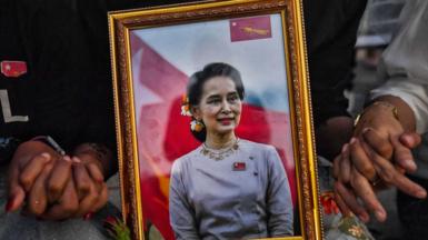 A picture of detained civilian leader Aung San Suu Kyi is seen as Myanmar migrants living in Thailand hold hands during a memorial in Bangkok on March 4, 2021 to honour those who died during demonstrations against the military coup in their homeland.