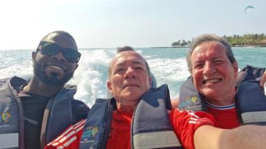 Yostin Mosquera (Left), Albert Alfonso (Middle) and Paul Longworth (Right) on a speedboat. They are wearing lifejackets and smiling at the camera. There is clear blue sea behind them with the wake of the waves. In the distance palm trees can be seen on the shore line. 