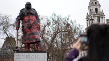 A woman takes photos of the statue of Sir Winston Churchill in Parliament Square, which has been defaced overnight with red paint.