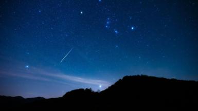 Blue night sky with Milky Way stars with Orionids meteor shower trails and countryside tree silhouettes