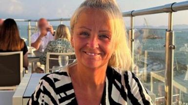 A general picture of Anita Rose. She is sat on balcony at a table and is smiling at the camera. People can be seen dining behind her. She has blonde hair that is tied up.