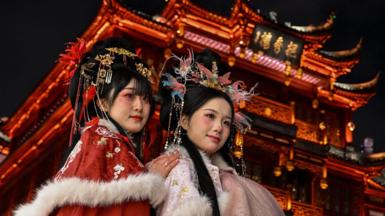 Women wearing traditional costumes pose for photographs in front of a Chinese temple