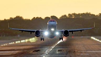 A plane takes off from London Gatwick airport in Crawley, West Sussex - the plane can be seen front a short distance off the ground, either about to land or take off - it is at sunset with the golden glow of the sun lighting up the area around the runway, with silhouetted trees in the background  