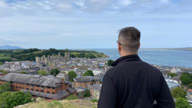Iwan Rhys yn edrych dros dref Caernarfon