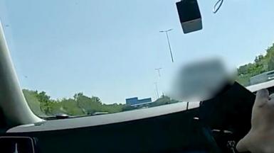 A hand holding a phone inside a car with a blurred out van in front on the road.
