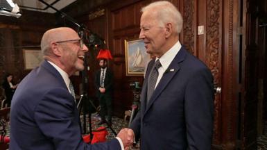 Joe Biden wears a dark blue suit and shakes hands with BBC journalist Nick Robinson