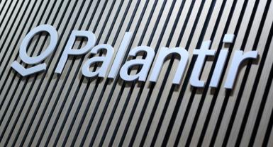 Close-up of the Palantir logo sign in white lettering mounted on a wall with vertical wooden slats in alternating light and dark tones.