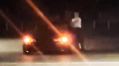 A car being driven at night with a man wearing a white tshirt hanging out of the side window