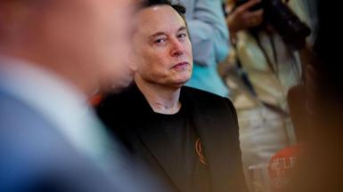 Elon Musk peers over at another person, looking unimpressed