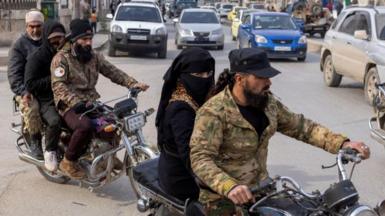 Two groups of people ride along a street on motorbikes in Idlib on 16 December