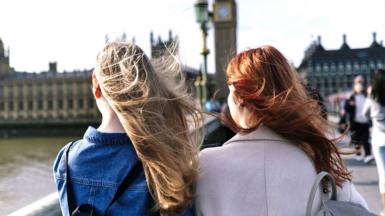 Two young women walk along Westminster Bridge in London with Parliament in the background