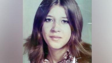 Laura Aimee, in a school photo from the 1970s. She has long brown hair parted down the middle and brown eyes, and wears a patterned blouse. 