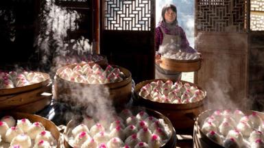A woman entering a room to add her latest creation to a mountain of steaming dim sum, prepared as part of a feast to celebrate Chinese New Year.