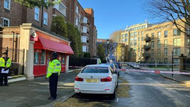 Two police officers stand behind police tape and in front of red-fronted newsagents