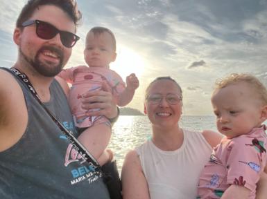 Nathan, his wife and their two children on holiday with a sunset over the sea behind them