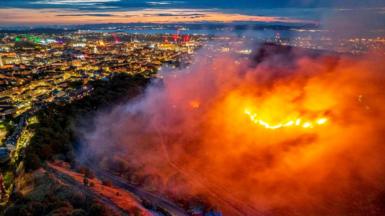 A line of fire on a hillside with the night time backdrop of Edinburgh