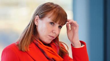 Angela Rayner wears a thoughtful expression and scratches her head. She is wearing a bright red coat