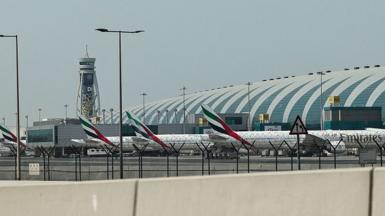 Three Emirates planes lined up at Dubai International Airport, a control tower stands in the background.