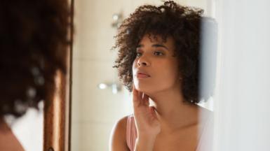 A woman, standing in front of a mirror, examining her eye wrinkles 