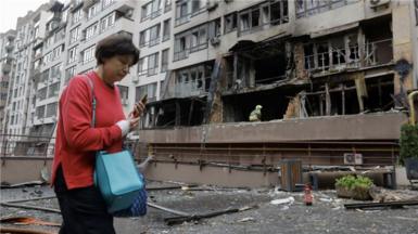 A woman walks past a bombed-out building