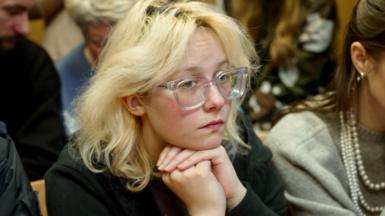 Diana Loginova sits with her head on her clasped hands in a court in St Petersburg, wearing glasses with transparent frames under her blonde hair
